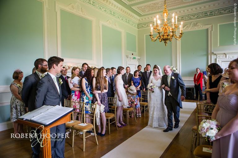 Bride escorted by father of the bride down the isle to her groom in the Green Room at Botleys Mansion Surrey