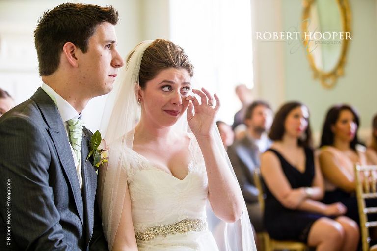 Bride wiping away tears during reading at her civil wedding ceremony in the Green Room at Botleys Mansion Surrey