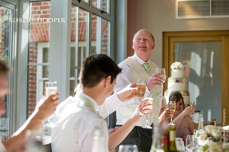 Father of the bride makes a toast during speeches at wedding breakfast in The Atrium at Botleys Mansion Surrey