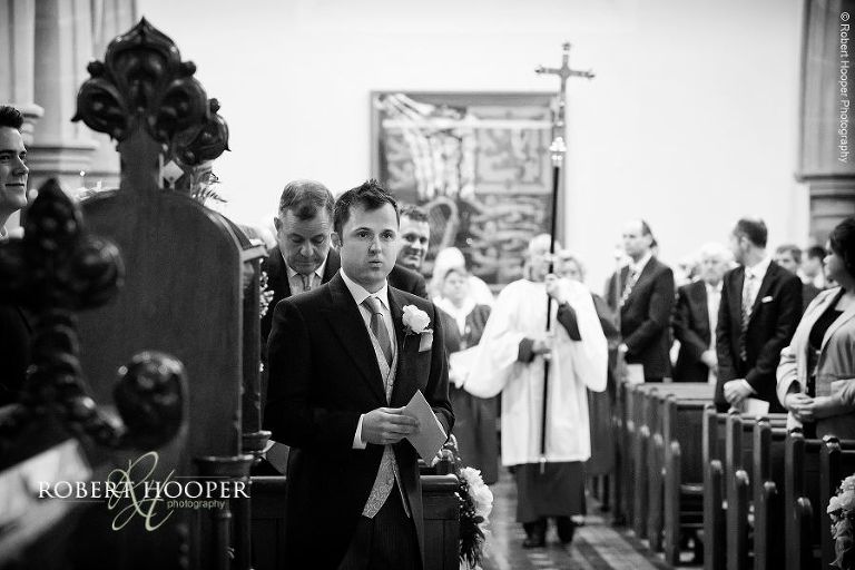 Nervous groom waiting at the alter for the arrival of the bride on their wedding day at St. Anne's Church and Farnham Castle in Surrey