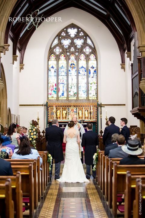 Bride, bride groom and father of the bride standing at the alter with the vicar at the beginning of marriage ceremony at St. Anne's Church Surrey