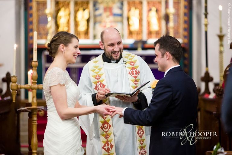 Bride and groom sharing a laugh with the vicar during their marriage ceremony at St. Anne's church Surrey