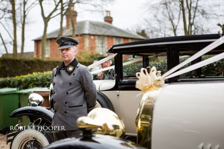 Driver of vintage car waiting to take bride and groom to wedding reception at Farnham Castle Surrey