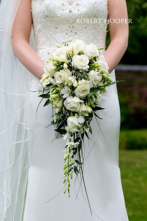 Bride's trailing bouquet of white freesia and roses held by the bride before her wedding ceremony at Oaks Farm Surrey