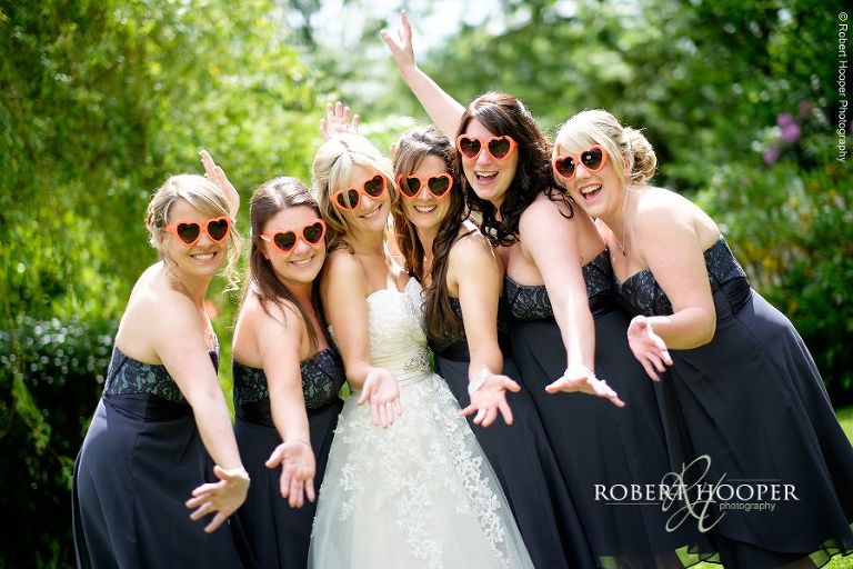 Bridesmaids in the garden on a sunny day wearing orange love heart sunglasses for wedding day at All Saints' Hordle Church Hampshire and The Three Tuns, Dorset