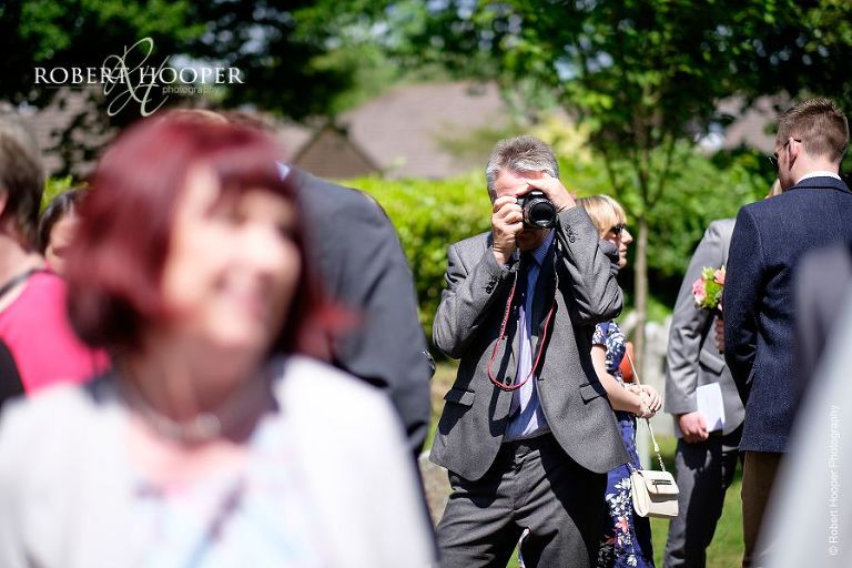 Wedding guest taking photographs of other guests outside the church after summer wedding ceremony at All Saints' Church Hordle Hampshire