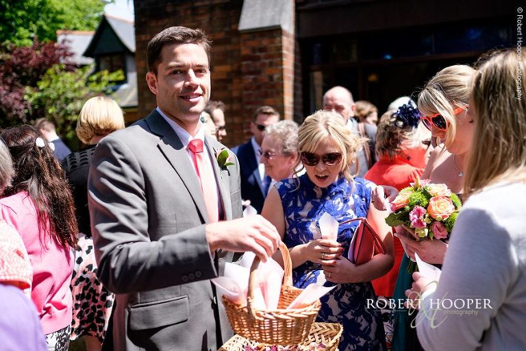 Groomsman passing round confetti to wedding guests after wedding ceremony outside All Saints' Church Hordle Hampshire