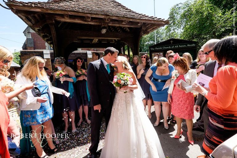 Bride and groom kiss after confetti throwing at the Lychgate of The Parish Church of All Saints, Hordle in Hampshire