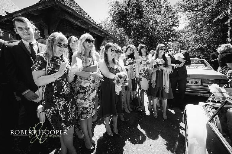 Wedding guests watching as newlyweds leave the church in vintage wedding car for wedding reception venue at The Three Tuns Dorset