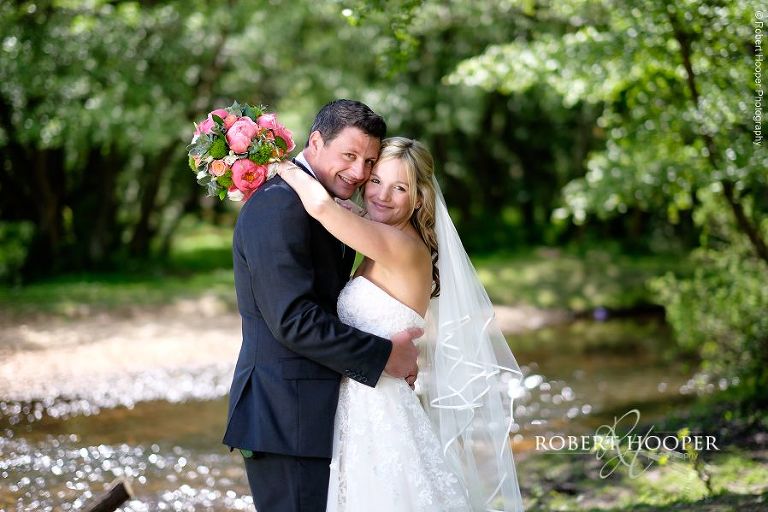 Bride holding beautiful pink and peach bouquet hugs her husband in the New Forest after their wedding at All Saints Hordle Hampshire