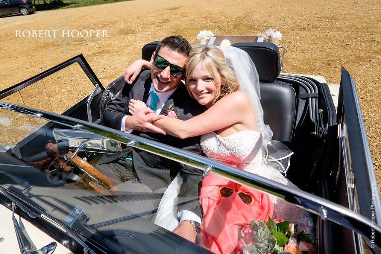Bride and groom hugging in vintage wedding car after getting married at All Saints Hordle Hampshire