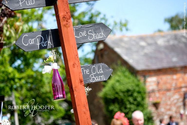 Signpost with pink bottle with bow and flowers on pointing guests in the right direction for summer wedding reception in the marquee in the garden at The Three Tuns Dorset