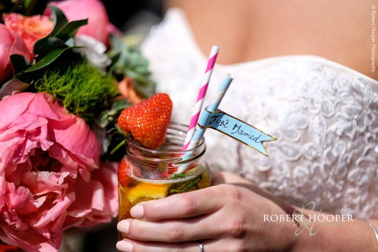 Glass of Pimms in a jar with a strawberry on the side and two straws with a just married sticker on one served to bride on arrival at her outdoor wedding reception at The Three Tuns Bransgore Dorset