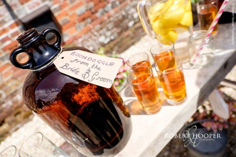 Demijohn of drink labelled "Boondoggle" from the bride and groom on drinks table at summer outdoor wedding reception at The Three Tuns Bransgore, Dorset