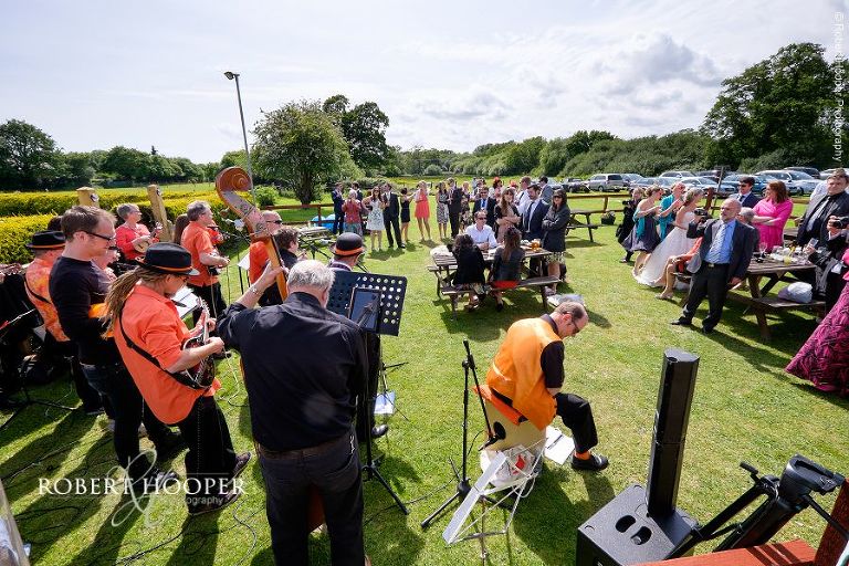 Wedding guests enjoying strings wedding band play at village fayre themed wedding reception in the gardens of The Three Tuns Bransgore Dorset