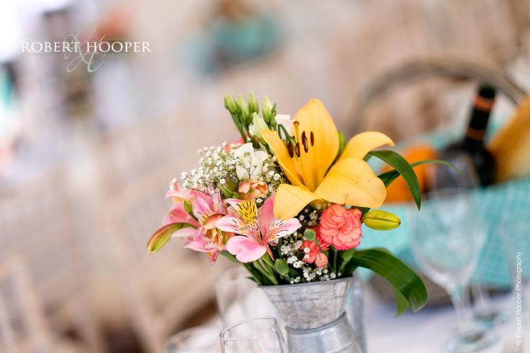 Simple flower arrangements in tin jugs on tables of village fete themed wedding reception in marquee at The Three Tuns Bransgore Dorset