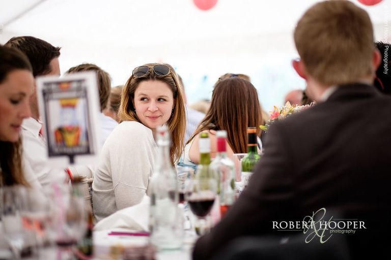 Wedding guest seated at long table in picnic style seating layout for village fete themed wedding reception in the marquee at The Three Tuns Bransgore Dorset