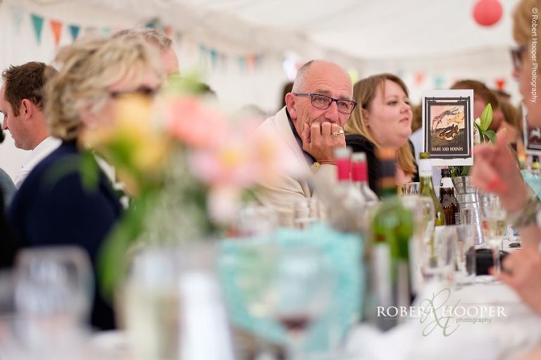 Wedding guest seated at long table in picnic style seating layout for village fete themed wedding reception in the marquee at The Three Tuns Bransgore Dorset