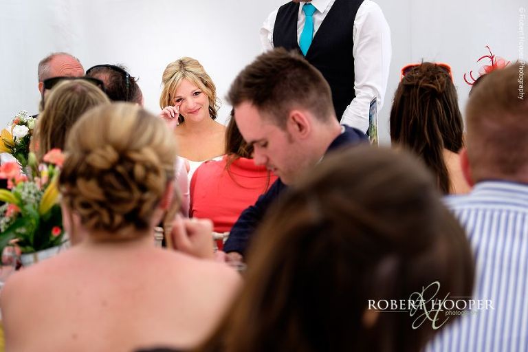 Bride looking across to her bridesmaid and shedding a tear during emotional speech by her new husband at their wedding breakfast in the marquee at The Three Tuns Bransgore Dorset