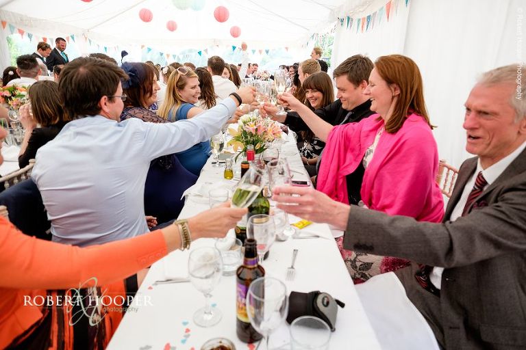 All wedding guests raising their champagne glasses in a toast to the happy couple at their wedding breakfast in the marquee at The Three Tuns Bransgore Dorset