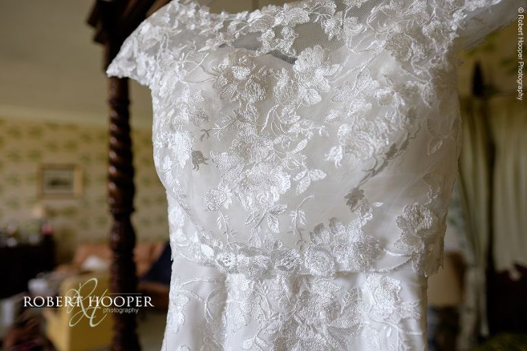 Lace wedding dress hanging from four poster bed in Earl of Northumberland suite at Eastwell Manor Kent