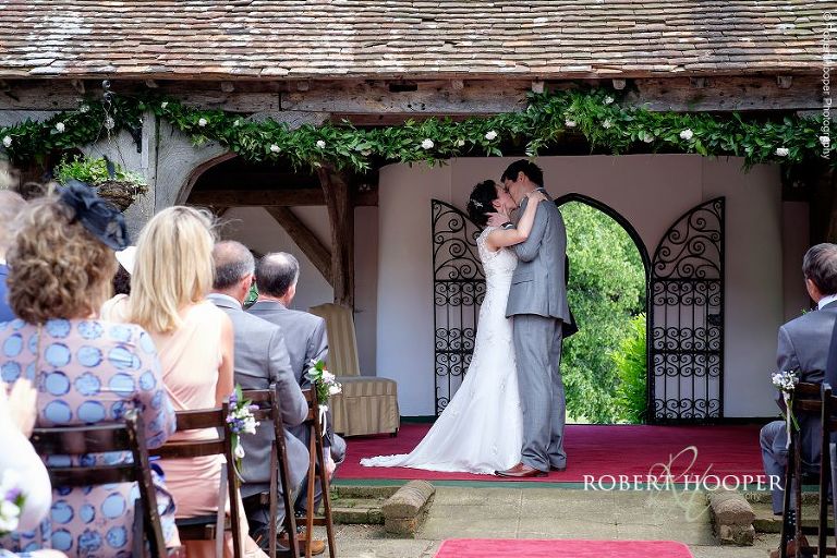 Bride and groom kiss having been pronounced man and wife following their outdoor wedding ceremony at Eastwell Manor Ashford Kent