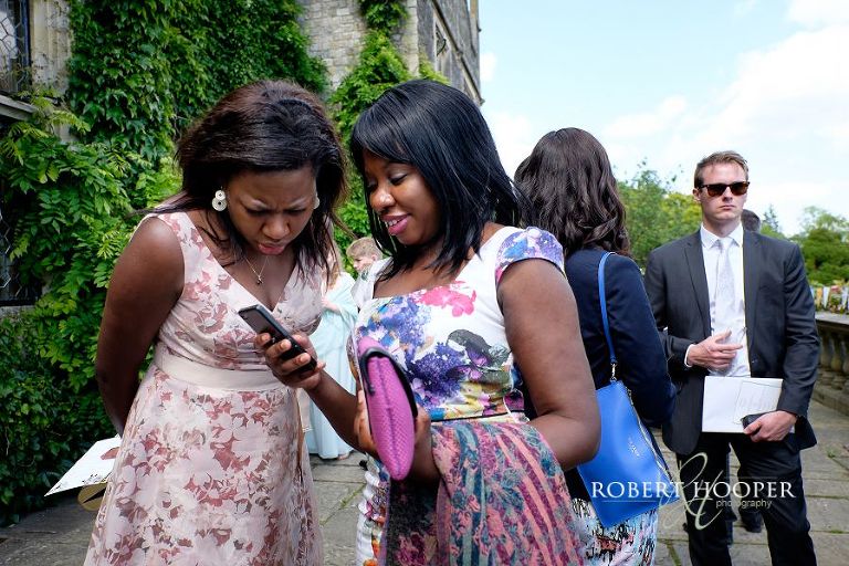 Wedding guests looking at their photos on their iPhone at reception drinks reception at Eastwell Manor Ashford Kent