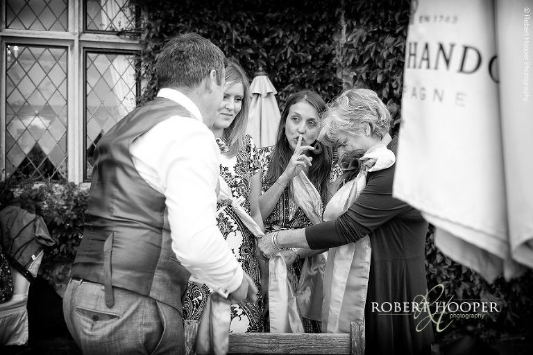Wedding guests dressing up in wedding chair sashes at drinks reception in the gardens at Eastwell Manor Ashford Kent