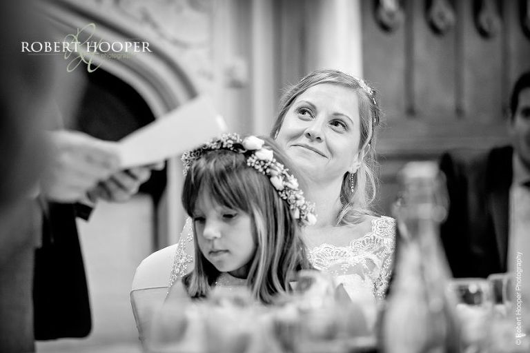 Bride looking affectionately at her new husband as he gives his speech at their wedding breakfast celebration in The Great Hall Horsley Towers Surrey