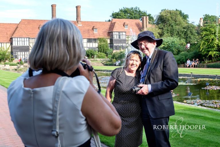 Wedding guests stop to take each other's photos in front of the main house at RHS Wisley on wedding day in August