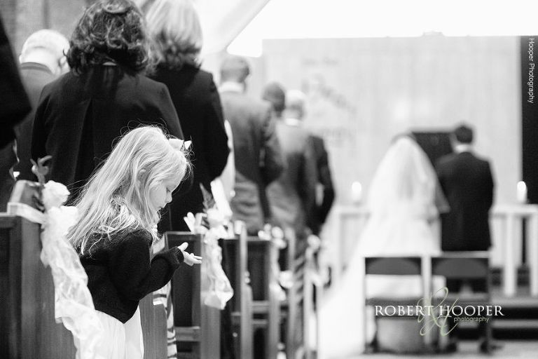 Little girl in church pew play with petals from isle in church on wedding day at St Joseph's Catholic Church Surrey