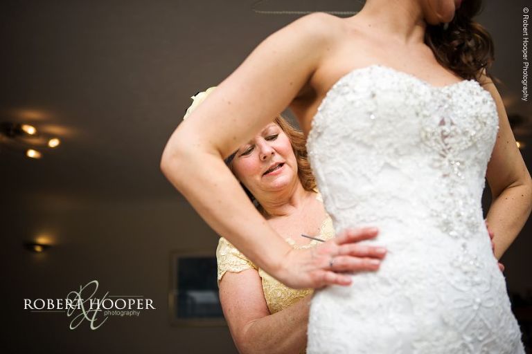 Mother of the bride buttoning up bride in to her wedding dress on wedding day at Bookham Baptist Church Surrey and Loseley Park, Guildford Surrey