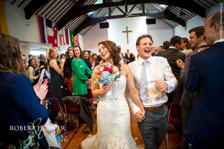 Bride and groom walk back up the isle as husband and wife whilst guests clap and celebrate at Bookham Baptist Church Surrey
