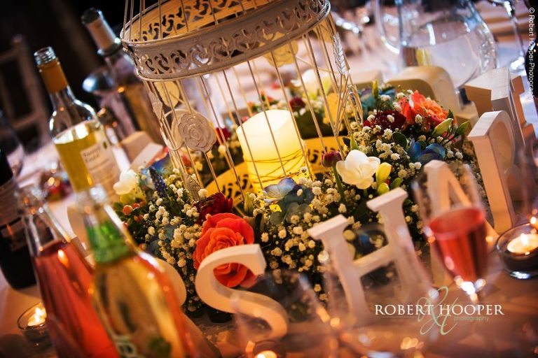 Wedding breakfast table decorated with colourful flowers, white bird cage, candles and letters "Mr and Mrs" for wedding reception in The Tithe Barn at Loseley Park Guildford Surrey