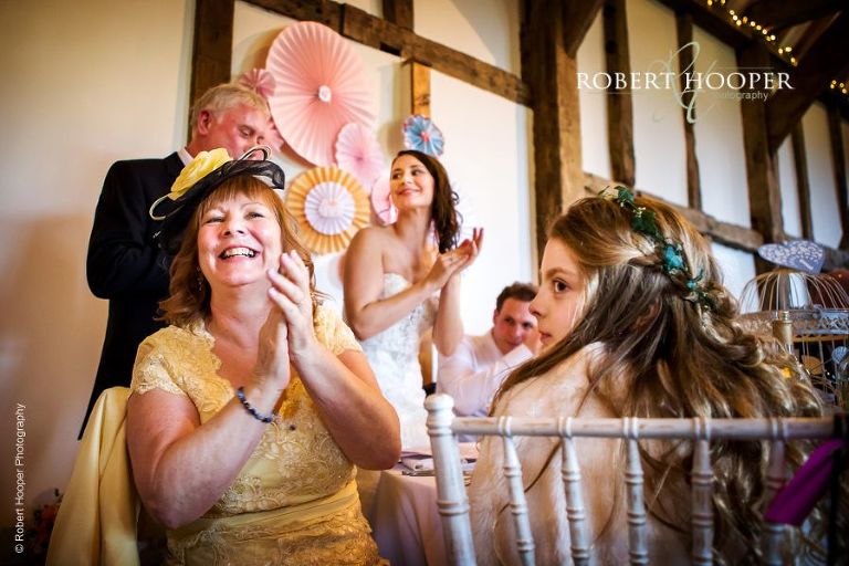 Mother of the bride clapping during speeches at wedding breakfast in Tithe Barn, Loseley Park in Surrey