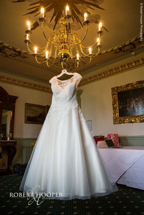 White chiffon and lace wedding dress hanging from chandelier ready for bride to wear for wedding day at Chilston Park, Maidstone in Kent
