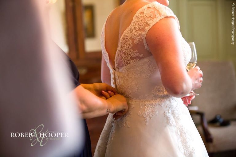 Bride's mother doing up back of wedding dress in preparation for wedding ceremony at Chilston Park, Maidstone in Kent