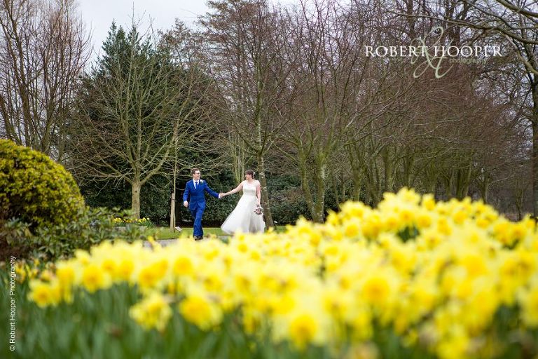 Bride and groom walk through the grounds amongst the blooming daffodils at Chilston Park in Kent