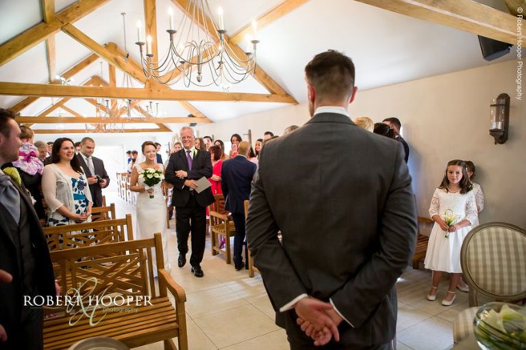 Bride coming down the isle in The Stables on her wedding day at Oaks Farm Barn Croydon Surrey