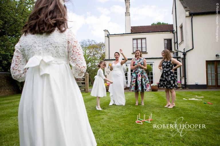 Bride, flower girls and wedding guests play lawn games on wedding day at Oaks Farm Barn Surrey