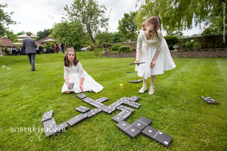 Flower girls play dominoes lawn game on wedding day at Oaks Farm Barn Croydon Surrey