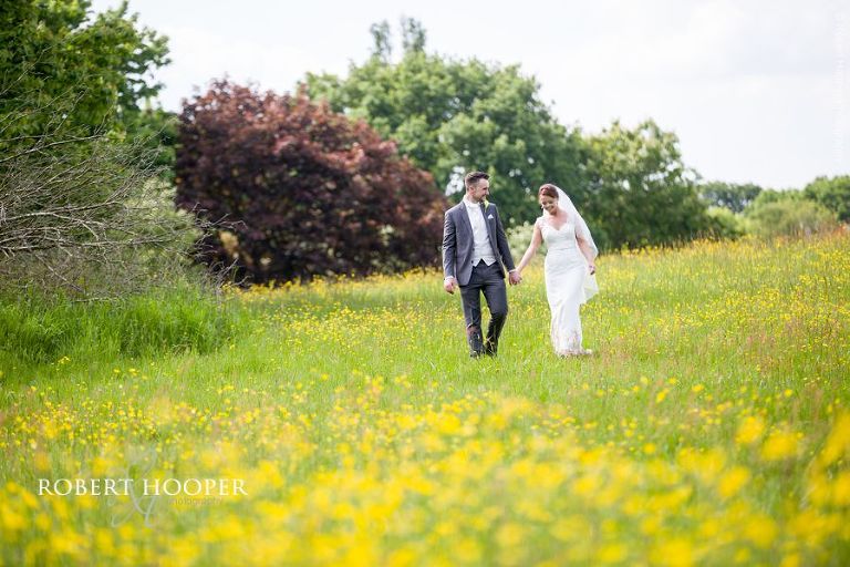 Bride and groom walk through buttercups in on their wedding day at Oaks Farm Barn Croydon Surrey
