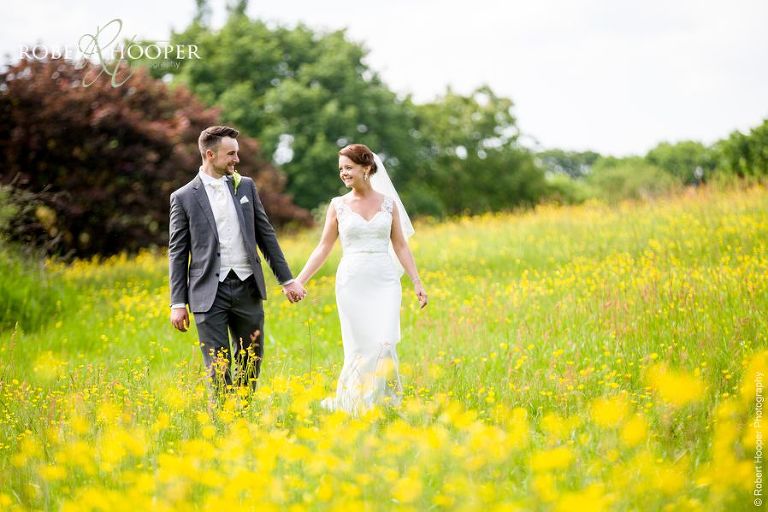 Bride and groom holding hands, walking through buttercups on their wedding day near Oaks Farm Barn Croydon Surrey