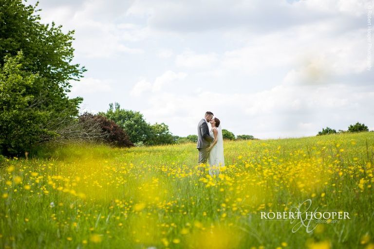 Bride and groom kiss in buttercup field on their wedding day near Oaks Farm Barn Croydon Surrey
