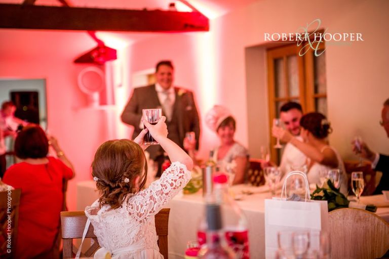 Flower girl toasts the bride and bride groom with her glass of coke during best man's speech at Oaks Farm Barn Shirley Surrey