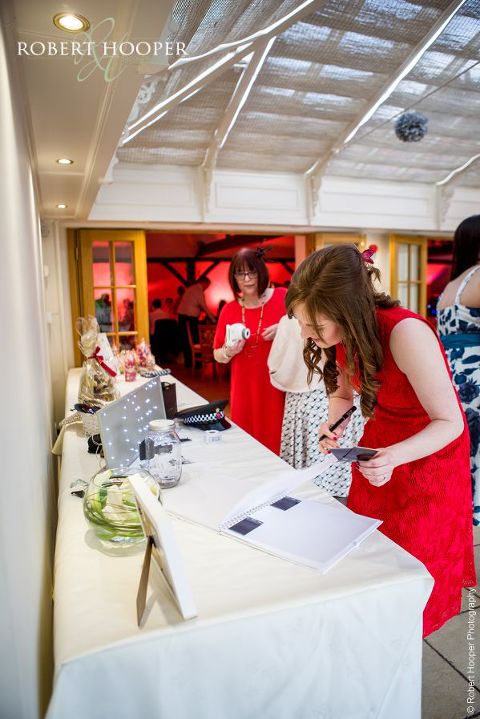 Wedding guests signing guest book and adding polaroids at wedding reception at Oaks Farm Barn Shirley Surrey