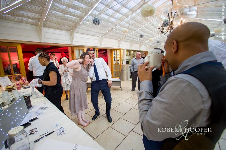 Wedding guests using face masks to take polaroids for guest book at Oaks Farm Barn wedding Surrey