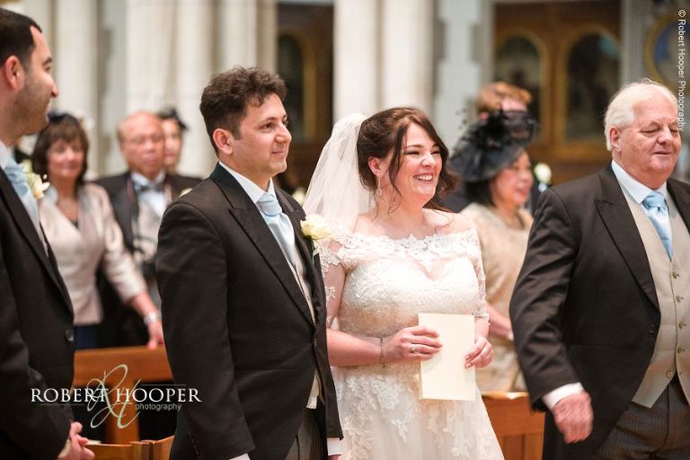 Bride and groom smiling at vicar during wedding ceremony at Sacred Heart Church Wimbledon London