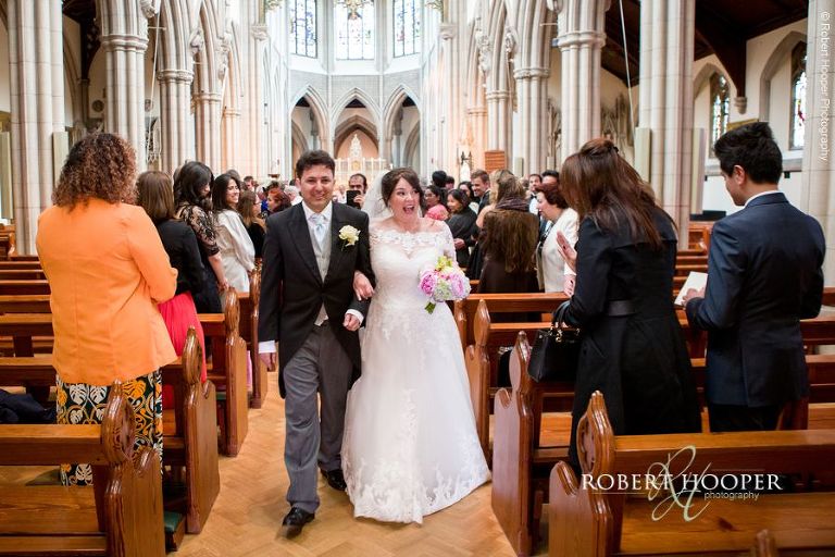 Bride and groom walk back up the isle as man and wife on their wedding day at Sacred Heart Church Wimbledon