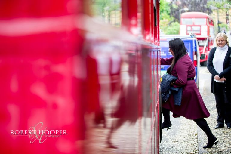 Wedding guests boarding red London bus to take them from Sacred Heart Church Wimbledon to Hampton Court House Surrey for wedding reception